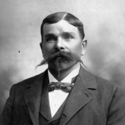 Head and shoulders studio portrait of Edgar L. Miller, Gunnison, Colorado; he wears a wool sack coat and collared vest with a bow tie; his hair is parted and neatly combed with rolled ends on his large mustache and beard.