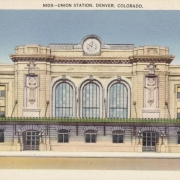 View of Union Station on 17th (Seventeenth) Street and Wynkoop Street in Denver, Colorado. The stone, classical building has a central clock, arched windows, a flat roof and a covered sidewalk.