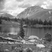 Two pine trees stand among large rocks on the near shore of Diamond Lake in Boulder County in This view looking toward Arapaho Peak in the distance on the border of Boulder and Grand counties in Colorado. Small  patches of snow are on Arapaho Peak.