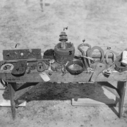 View of artifacts found at Fort Caspar in Casper (Natrona County), Wyoming. Shows harness and farrier's tools including a fish plate (from a freighter wagon), a hame and short tug, an axe, a coupling iron, a spoon, a glue pot, a yoke iron, part of a musket, a bolster iron, a telegraph insulator, a wagon hub, and horse, mule and oxen shoes.