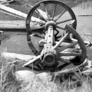 A set of wagon wheels sits half submerged in the water on the edge of Lost Lake west of Eldora in Boulder County, Colorado. A portion of the nearer wheel is missing. Pieces of wood float near the set of wheels.