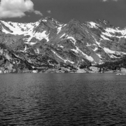 Silver Lake stands in the foreground in Boulder County, Colorado,  with a ridge of mountains in the distance. Tall pine trees stand on the far shore of the lake. Patches of snow are on the distant peaks. Large clouds are in the sky.