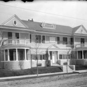 A round porch stands on each end of the large residence of Judge Henry T. Rogers at 1739 East 13th (Thirteenth) Avenue in Denver, Colorado. Shutters hang from the windows on the house. Columns support the portico. A round window on the front door has "1739" painted on it.