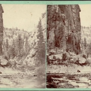 A man sits on a rock in the middle of probably Middle Boulder Creek, and a dog lies beside the creek in the narrow canyon. Shows a sheer rock wall, trees and fallen logs in the creek bed in Boulder County, Colorado.