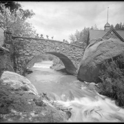 Rock footbridge crossing Fountain Creek to Soda Spring pavilion, Manitou Springs, Colorado; shows men and women standing on bridge.