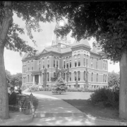 Exterior view of Boulder, Colorado, County Courthouse located between 13th (Thirteenth) and 14th (Fourteenth) Streets on Pearl Street; designed by Frank E. Edbrooke and constructed in 1883; shows men resting on park bench with bicycle in left foreground and scaffolding and ladder on courthouse walls.
