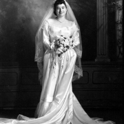 Studio wedding portrait of María Oralia "Orie" Durán Trujillo of Denver, Colorado. She wears a long, silk wedding gown with a scoop neck, trimmed in lace, a veil trimmed in lace and holds a bouquet of flowers. María married Filbert G. Trujillo, sang in the Saint Cajetan's church Mariachi Alegre de San Cayetano, and directed the Southwest Hispanic Colonial Dancers.