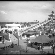 View of ride called the Shoots, "White City" (later called Lakeside Amusement Park), Lakeside, Colorado, near Denver; shows two cars ascending ride and one car descending, a group standing on bridge near Casino Theater watching the ride, and various booths around base of ride (cigars, palmistry). Edge of ferris wheel is center.