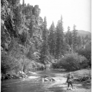 One man fishing in South Platte River in Platte Canyon possibly near Glenisle, Colorado, reached via Colorado and Southern Railway; fisherman casting into stream with wicker creel on shoulder.