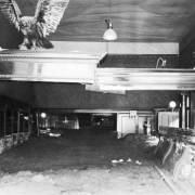 Interior of Sheridan Hotel Bar with mud and high-water marks from  the disastrous Cornet Creek flood on July 27, 1914, Telluride, Colorado. Calendar on back wall marks date; room includes a clock high on left wall, stuffed bird with outstretched wings on top decorative molding, bar, cash register, and electric lights.