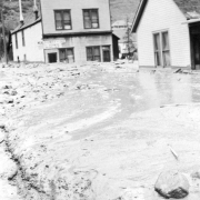 View north up mud and debris-filled street from the disastrous Cornet Creek flood on July 27, 1914, Telluride, Colorado; shows two-story false front, Iowa House on corner, and residence across street.
