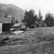 Street scene after the Cornet Creek flood on July 27, 1914, Telluride, Colorado. Mud and debris fill street with damaged wood-frame structures; Miner's Union Headquarters and Hospital are in background.