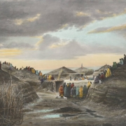 North American Indian (Pawnee) men and women sit and stand on and near earthen lodges at sunset probably in Nebraska. They are wrapped in blankets. Shows fences made of twigs or brush, and a plaza with an American flag that flies near the entrance to a lodge.