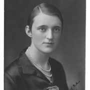 A studio portrait of Grayce Smith a possible student at North High School and a member of the Kismet Club.  She has her hair slicked back and is wearing a black stain top with white lace pinned to it.  She wearing a triple strand pearl necklace.
