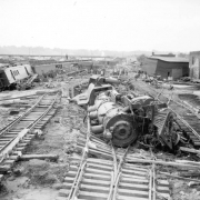 Men remove mud, the result of a flood, from railroad tracks at the Denver and Rio Grande Western Railroad roundhouse in Pueblo, Colorado. Shows a locomotive, an overturned railroad car, freight cars, stock cars, passenger cars, baggage carts, and debris. Dead cows are in the stock car doorways and on the ground. Signs on the stock cars read: "Missouri Pacific," "12396," and "51492." Shows footprints in the mud.