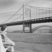 View of the Triborough Bridge and the Hell Gate Railroad Bridge in the borough of Queens, New York City, New York. A woman in uniform and garrison cap sits on a bench in Astoria Park.