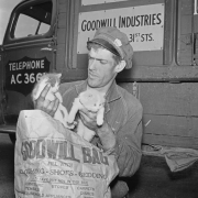 A Goodwill delivery man holds kittens and a bag in Denver, Colorado; his bag lists items acceptable for donation. Letters on his truck read: "Rehabilitation and Employment of Handicapped Persons."
