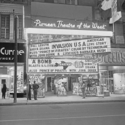 View of the Tabor Theater entrance at 1014 16th (Sixteenth) Street in Denver, Colorado. Signs and marquee read: "Pioneer Theater of the West," "Invasion U.S.A.," "Prince of Pirates," "A Bomb Blasts in U.S. Cities," and "Highlander Blue and Gold Drill Team." Feltman & Curme and Leed's Shoe stores are to the sides.