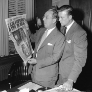 Scott Brady, star of "Canon City," and Palmer Hoyt, editor and publisher of the Denver Post from 1946-1971, with a Denver Post newspaper, look at the headlines in an office in Denver, Colorado. A sheet with "The Denver Post Deadline Schedule" sits on the desk. The headline, about the 1947 prison break on which "Canon City" was based, reads: "2 Slain, 9 Captured, In State Pen Break, Stir Crazy Cons Lead Pen Break."