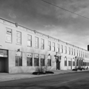 View of a brick commercial building at the corner of 25th (twenty fifth) and Curtis Street, in the Curtis Park Neighborhood of Denver, Colorado; features include a portico, parapet, dark brick coursing and corbels Stone lintel reads: "Ideal;" entry awning reads: "Eric's Pub."
