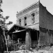 View of the home of Justina Laurena Carter Ford, M.D., Denver's first African American woman doctor, at 2335 Arapahoe Street, in the Five Points Neighborhood of Denver, Colorado. The abandoned brick house has a covered porch, brick ornaments, and a wooden cornice.