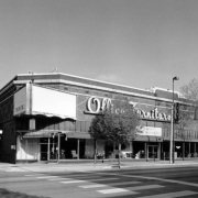 View of a two story brick retail building at 21 South Broadway Street in the Baker Neighborhood of Denver, Colorado. Features include ceramic trim, storefront windows, and a metal and neon sign: "Office Furniture."