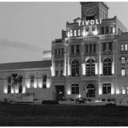 Night view of the Tivoli Brewery Building (formerlyTivoli-Union Brewery) at 10th (Tenth) and Larimer Streets in the Auraria neighborhood of Denver, Colorado. The four-story brick building has arched windows, a smokestack, and a tower with a mansard roof. A sign reads: "Tivoli Beer."