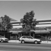 View of storefronts at 30-32 South Broadway Street in the Speer Neighborhood of Denver, Colorado. The brick and stone buildings have tile or stone cladding. Signs read: "Foot Clinic," "Sandwich Shoppe," and "Law Building."