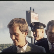 Pat Boone, a singer and actor, poses with an unidentified man, probably in Denver, Colorado.  A Colorado State trooper is nearby.