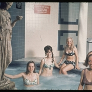 Women in two piece bathing suits pose on or in a jacuzzi type mineral bath in the club house of the Green Mountain Townhouses in Lakewood (Jefferson County), Colorado. A reproduction of a classical style statue of a woman is beside the pool. A sign reads: "Hydro-Swirl Mineral Pool 3 to 5 Minutes in This Pool is Sufficient." The walls are tiled. Shows a trash container and an aluminum and plastic chair.