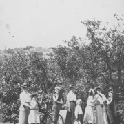 Members of the William S. Jackson family pose with a boy on a bicycle on a path probably near South Cheyenne Canyon in El Paso County, Colorado. From right to left: Possibly Aunt Mamie, Edith, William (1889-1981), on the bicycle, Roland, Mary C. Banfield, Gardner, possibly Helen, and an unidentified woman and Everett. The women wear long skirts and blouses and hats. The girls wear dresses and hats. The boys have on short sleeved shirts, short pants and caps. Most of them cover their mouths.