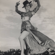 Louise Campa, Lucille Campa, a well known dancer and teacher of Mexican, Spanish classical dance and flamenco, poses in a classical style Spanish dance costume. She wears a short blouse with long sleeves, has a bare midriff and has a short skirt with a long train. She wears a Spanish style wide brimmed hat and holds castanets. Louise Campa was the wife of Professor Arthur L. Campa, Sr., and author, renowned scholar, historian and professor of cultural anthropology.