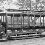 An engineer and conductor pose on a trolley car, identified as part of the South Broadway Cable Line, in Denver, Colorado. Lettering on the open-air trolley car reads: "Broadway."