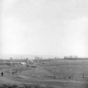 View of South Broadway at Alameda Avenue in Denver, Colorado. A man walks on the dirt road. A house is in the distance.
