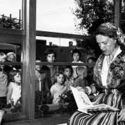Boys and girls look into a window at Geraldine Davies at the Ross-Broadway Branch of the Denver Public Library in the Speer neighborhood of Denver, Colorado. Her outfit includes paisley scarves and pearls.