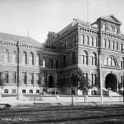 View of East Denver High School at 19th (Nineteenth) and Stout Streets in downtown Denver, Colorado; the Beaux Arts structure features mansard roof, pediments, bracketed cornices, arched windows and entry.