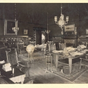 A view of the library in the Denver, Club at 17th (Seventeenth) and Glenarm in Denver, Colorado. The interior has upholstered wooden chairs, tables, bookcases, paintings in gilded frames, chandeliers, and a fireplace.