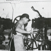 Interior view of a Great Western Sugar processing facility in Brighton (Adams County), Colorado; a man works with a wheel valve by a sign: "Danger - Bring Centrifugal To A Complete Stop Before Putting Discharger Into The Sugar."