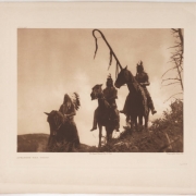 Native American (Crow) men on horses wear feather headdresses and braids. One holds a coup stick or staff.