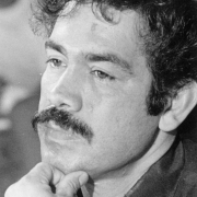 Portrait of Rodolpho "Corky" Gonzales, political activist and founder of the Crusade for Justice. Mr. Gonzales has a moustache and curly hair, and he rests his chin on his hand.