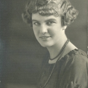 Elizabeth Kieffer poses for her South High School senior portrait in Denver, Colorado. Adler's hair is styled in a wavy bob with bangs and she wears a scooped neck blouse with a beaded flower, and probably a bead necklace.