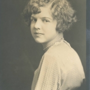 Anna May Bornhauser poses for her South High School junior portrait in Denver, Colorado. Bornhauser's hair is styled in a wavy bob and she wears a woven long sleeved blouse and a pearl necklace.