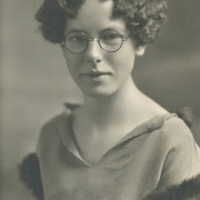 Viola Irene Flatt poses for her South High School junior portrait in Denver, Colorado. Flatt's hair is styled in a wavy bob and she wears round eye glasses and a blouse with fur trim on the sleeves and the back of the collar.