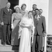Posing on the church steps in Keota, Weld County, Colorado, This wedding party wears suits, ties, gloves, boutonnieres, corsages, lace hats and veils. The groom has several teeth missing.
