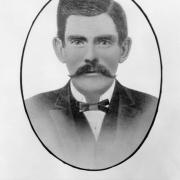 Portrait of John H. (Doc) Holliday. He wears a coat and bow tie. He has a moustache and parted hair with a cowlick.