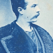 Studio portrait (profile) of probably Alfred G. Rogers, a mining agent and resident of Georgetown (Clear Creek County), Colorado. He wears a buffalo skin overcoat with wide lapels bound in leather, a vest and a tie and stickpin. His dark hair is parted on the side and he has a mustache.