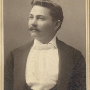 Studio portrait of Frank A. Franklin, a traveling salesman for a paper company in Denver, he probably visited Georgetown (Clear Creek County), Colorado. He wears a tuxedo with wide lapels, a shirt front and white bow tie. He has his hair parted in the middle and has a mustache.