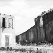 View of a disassembled sidewalk leading up to the ruins of the old court house, Breckenridge, Colorado; features a single leaf door with  decorative moulding and a wood beam running from the ground to the top of the building; other dilapidated buildings are near the court house.