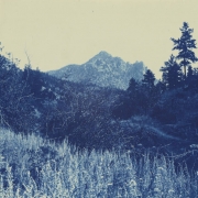 View of grasses and brush in a valley in the foothills of Jefferson County, Colorado. Shows rocks on slopes, and a trail. The rocky summit of Cathedral Spires is in the distance.