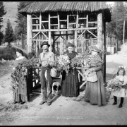 Women, a man, and a girl pose in Nast (Pitkin County), Colorado (west Hagerman Pass reached via Colorado Midland Railway), with wildflowers, fishing rods, a wicker creel, and fish. Outfits include wide brimmed straw hats and pleats; a rustic log gazebo and dog are in the background.